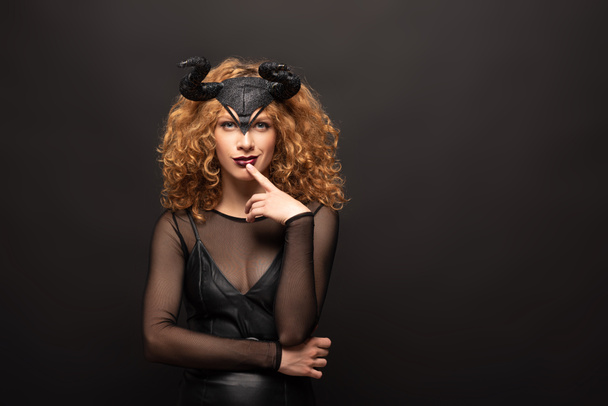 beautiful pensive woman posing in halloween costume with horns on black  - Фото, изображение