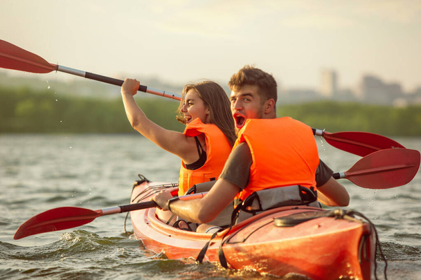 Happy couple kayaking on river with sunset on the background - Photo, image