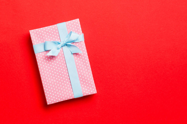 verpakt Kerstmis of andere met de hand gemaakte vakantie cadeau in papier met blauw lint op rode achtergrond. Aanwezig doos, decoratie van geschenk op gekleurde tafel, bovenaanzicht met kopieerruimte - Foto, afbeelding