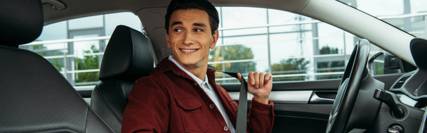 Lächelnder junger Mann mit Sicherheitsgurt im Auto, Panoramaaufnahme - Foto, Bild