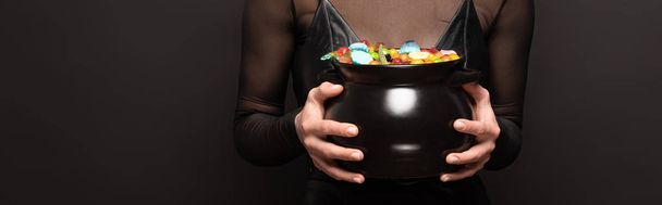 Teilansicht einer Frau, die einen Topf mit Süßigkeiten für Halloween auf Schwarz hält - Foto, Bild