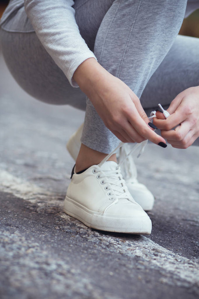 chica sentada en cuclillas para atar cordones de zapatos en zapatillas blancas en asfalto carretera, otoño deporte concepto al aire libre
 - Foto, Imagen