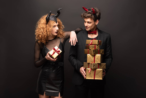 beautiful couple posing in halloween costumes with gift boxes on black - Foto, Imagem