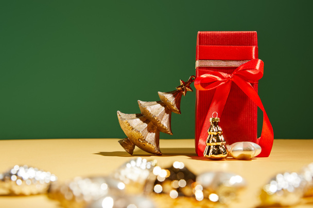 selective focus of red gift box and decorative Christmas tree with golden baubles on green background - Valokuva, kuva