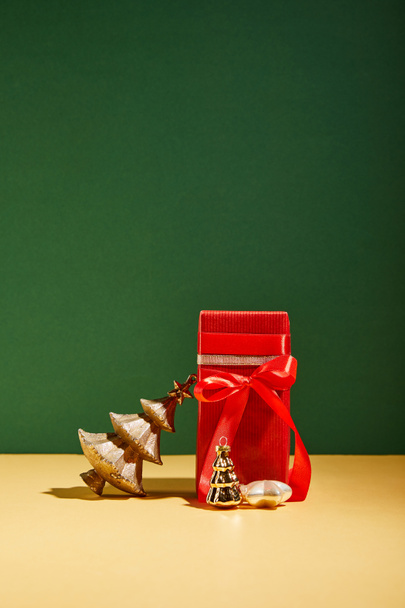 red gift box and decorative Christmas tree with golden baubles on green background - Foto, imagen