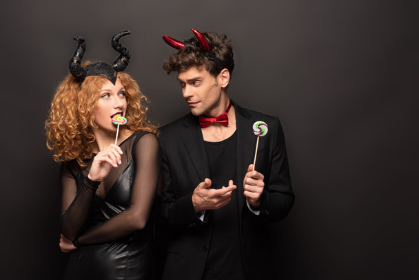 beautiful couple in halloween costumes holding lollipops on black - Photo, Image