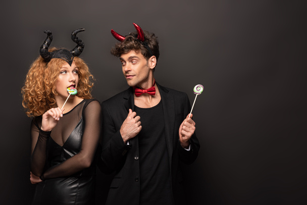 beautiful couple posing in halloween costumes with sweet lollipops on black - Foto, Imagem