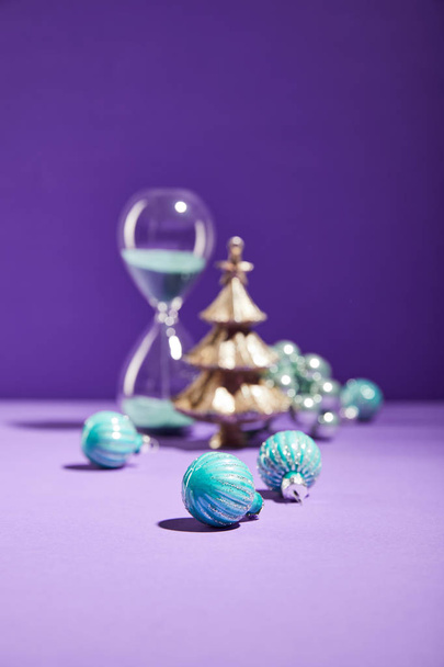 selective focus of decorative Christmas near blue baubles and hourglass on purple background - Zdjęcie, obraz