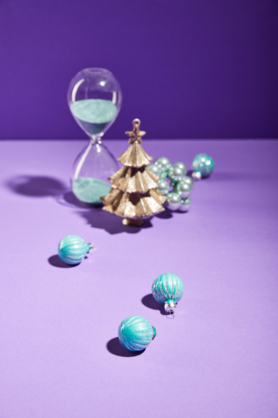 selective focus of decorative Christmas near blue baubles and hourglass on purple background - Valokuva, kuva
