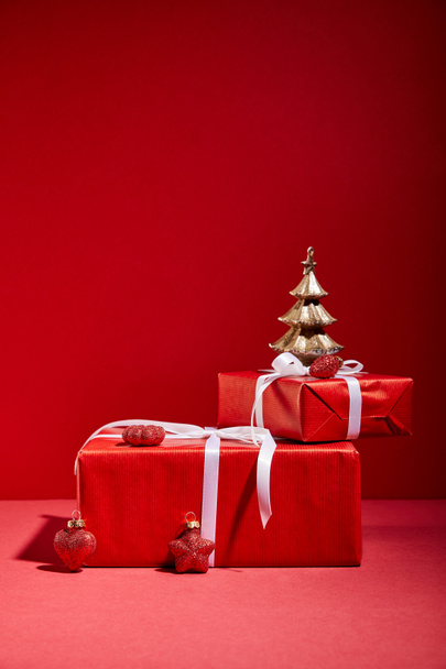 red gift boxes and decorative golden Christmas tree with baubles on red background - Фото, зображення