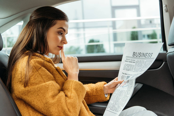 Pensive young woman reading newspaper on back seat of taxi - Foto, Imagen