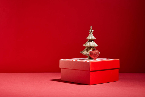 kırmızı hediye kutusu ve dekoratif altın Noel ağacı kırmızı arka planda takılı - Fotoğraf, Görsel
