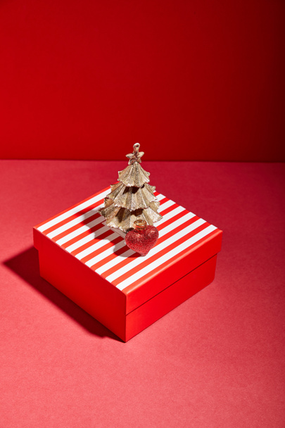 striped red gift box and decorative golden Christmas tree with bauble on red background - Fotografie, Obrázek