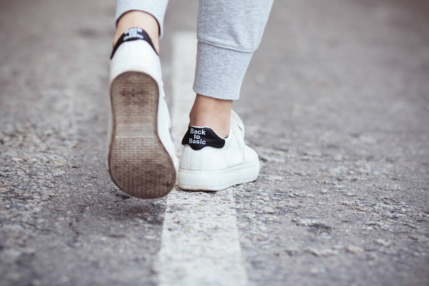 foots of a young woman in a white sneaker making step on a asphalt, concept of sport and body care - Photo, Image
