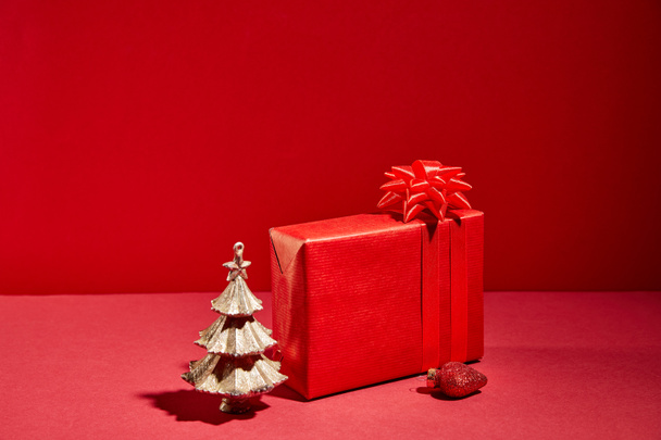 red gift box and decorative golden Christmas tree with bauble on red background - Foto, imagen