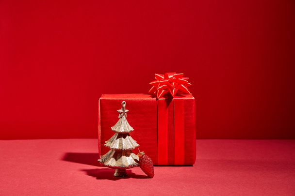red gift box and decorative golden Christmas tree with bauble on red background - Photo, image