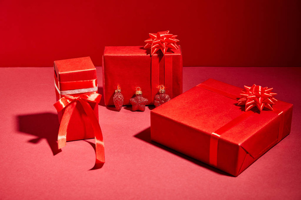 red wrapped festive gift boxes with ribbons and bows on red background - Fotó, kép