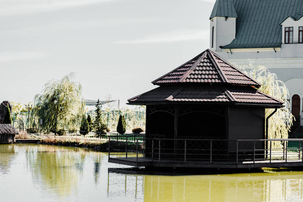 池の近くの建物や動物園の木の屋根の上の日光  - 写真・画像