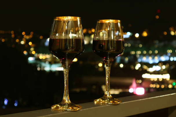 Dois copos de vinho na varanda com vista turva da noite da cidade no fundo
 - Foto, Imagem