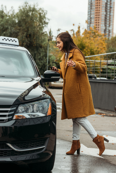 Mujer joven sosteniendo teléfono inteligente y hablando con el taxista al lado del coche
 - Foto, imagen