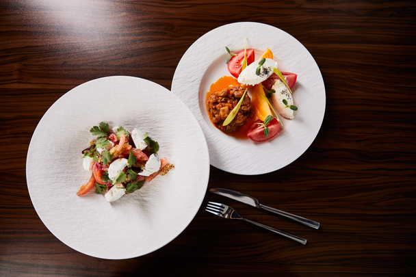 vista superior del delicioso plato del restaurante con caviar de berenjena y tomates y ensalada en mesa de madera con tenedor y cuchillo
 - Foto, Imagen
