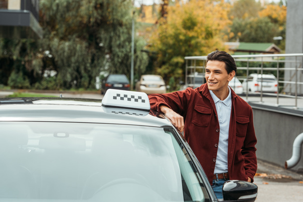 Glimlachende taxichauffeur kijkt naar weg naast de auto - Foto, afbeelding