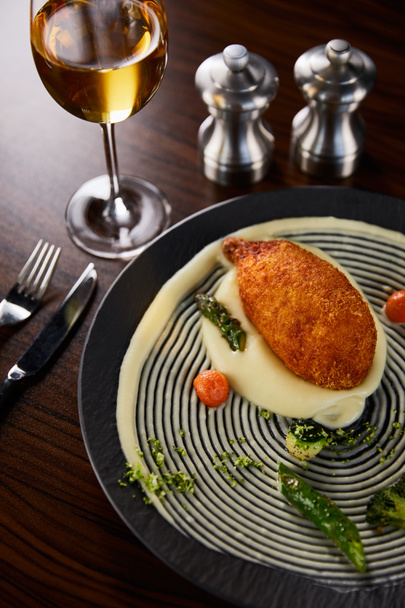 вкусный куриный киев и картофельное пюре подается на тарелке возле столовых приборов и белого вина
 - Фото, изображение