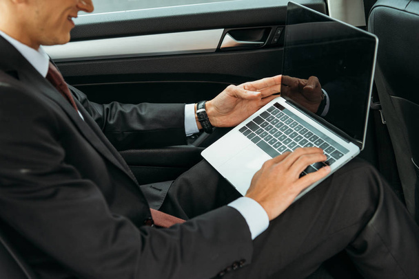 Oříznutý pohled na podnikatele pomocí notebooku s prázdnou obrazovkou v taxi - Fotografie, Obrázek