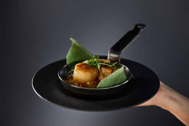 cropped view of woman holding plate with delicious grilled scallops on black background - Fotó, kép
