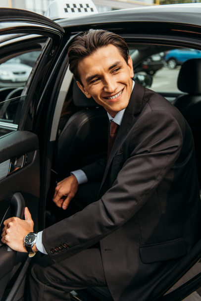Lächelnder Geschäftsmann steigt aus Taxi und schaut weg - Foto, Bild