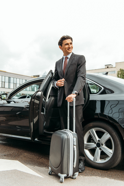 Smiling businessman with suitcase standing by taxi - Foto, imagen