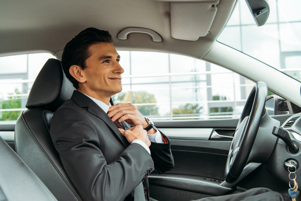 Hombre de negocios sonriente ajustando la corbata y mirándose en el espejo del coche no tripulado
 - Foto, imagen