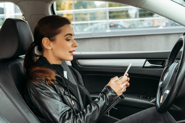 Mujer joven usando el teléfono inteligente en el asiento del conductor del coche no tripulado
 - Foto, imagen