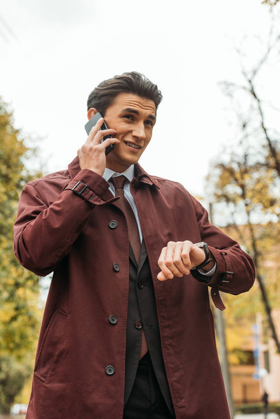 Liikemies puhuu älypuhelimella ja tarkistaa aikaa rannekellon kadulla
 - Valokuva, kuva