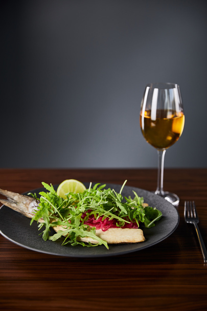 tasty restaurant fish steak with lime and arugula on wooden table near fork and white wine on black background - Fotografie, Obrázek