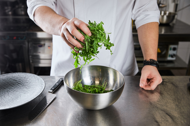 vista ritagliata dello chef che cucina insalata con rucola in cucina nel ristorante
 - Foto, immagini