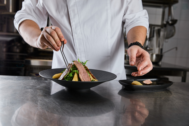 partial view of chef making dish with arugula, meat and potato at kitchen in restaurant - Photo, Image