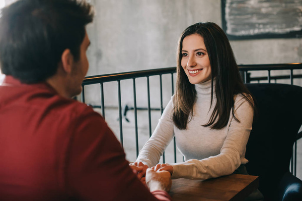 smiling young woman looking at boyfriend and holding his hands on balcony in coffee shop - Photo, Image
