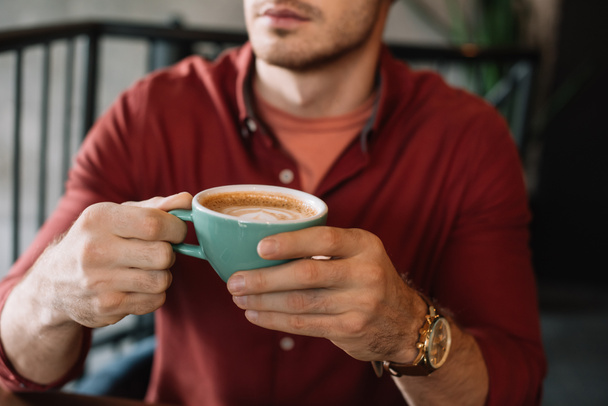 Ausgeschnittener Blick auf jungen Mann mit Tasse leckerem Cappuccino im Café - Foto, Bild