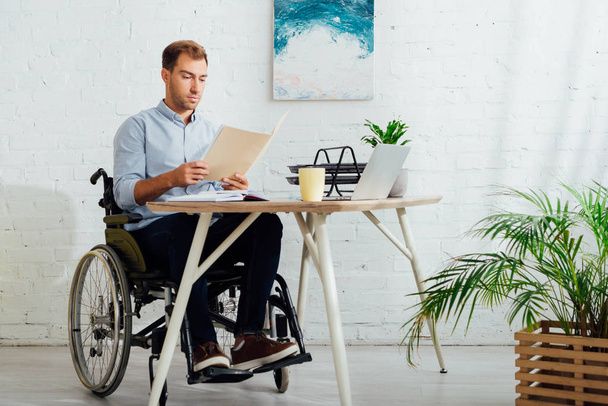 Man in wheelchair looking at papers at workplace - Fotó, kép