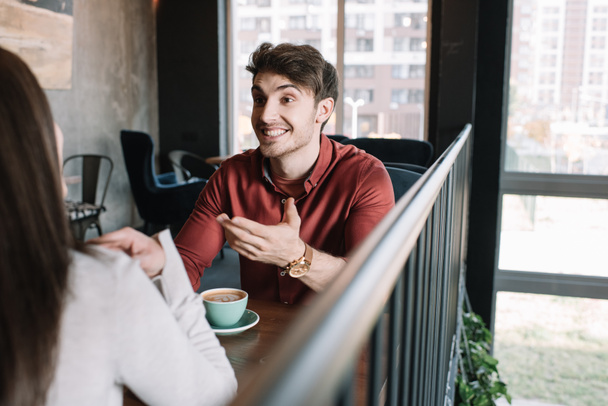 cheerful man talking to girl while drinking coffee on balcony in coffee shop - Photo, Image