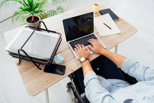 Rajatut näkymät mies pyörätuolissa kannettavan tietokoneen tyhjällä näytöllä työpaikalla
 - Valokuva, kuva