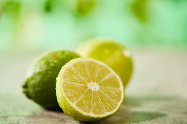 selective focus of whole and cut limes with drops on marble surface  - Foto, Bild