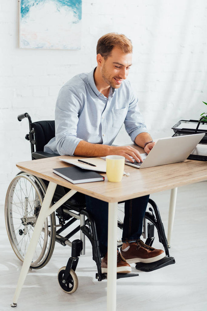 職場でノートパソコンのキーボードを入力する車椅子の幸福男 - 写真・画像