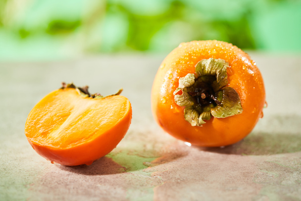 selective focus of whole and cut persimmons on marble surface  - Foto, Bild