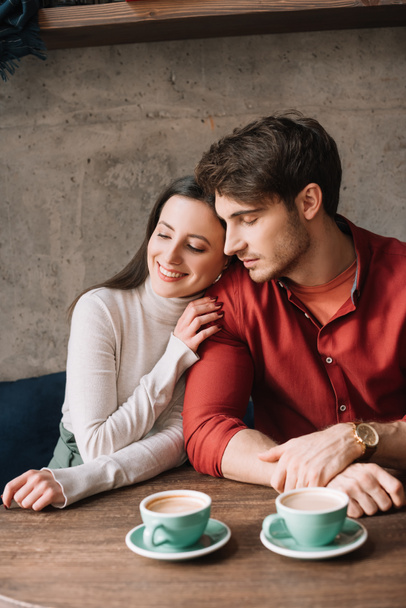 smiling tender young couple hugging and drinking coffee in coffee shop - Foto, imagen
