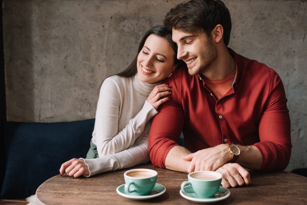 smiling romantic young couple hugging and drinking coffee in coffee shop - Photo, Image