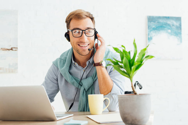 Smiling call center operator in wheelchair talking on headset at workplace - Foto, Imagen