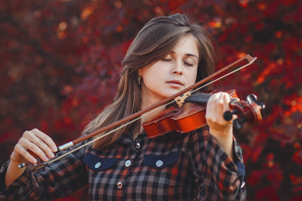 autumn portrait of romantic girl playing violin on a background of red foliage, young woman performance on nature, a concept of hobby and art - Photo, Image