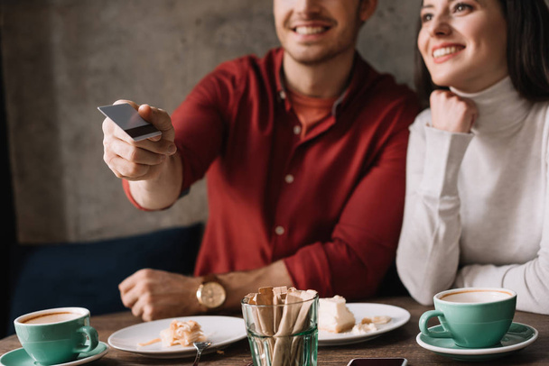 vista ritagliata di giovane coppia seduta in caffetteria mentre l'uomo in possesso di carta di credito
 - Foto, immagini